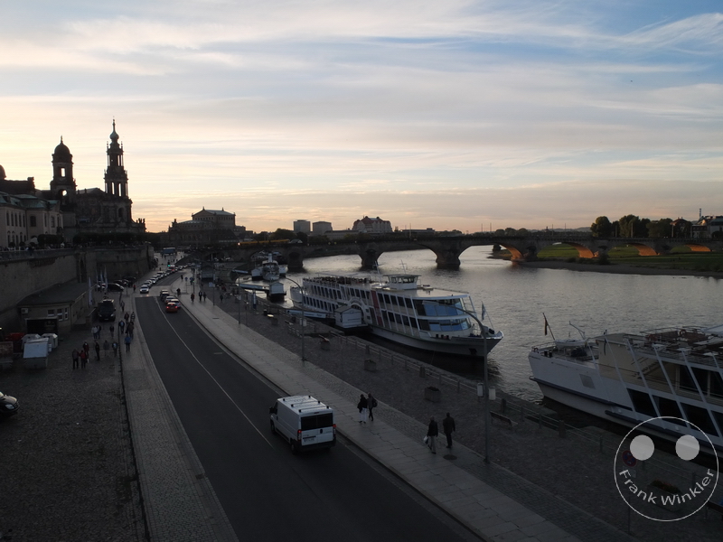 Deutschland - Dresden - Brühlsche Terrasse - Elbe - Flusspromenade bei Sonnenuntergang, Boote, Straße, Gehweg, historische Gebäude, Brücke im Hintergrund.