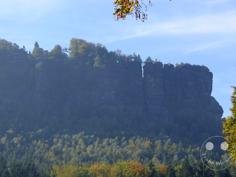 Deutschland - Sächsische Schweiz - Felsmassiv mit Bäumen, vertikaler Spalt und blauer Himmel im Hintergrund.