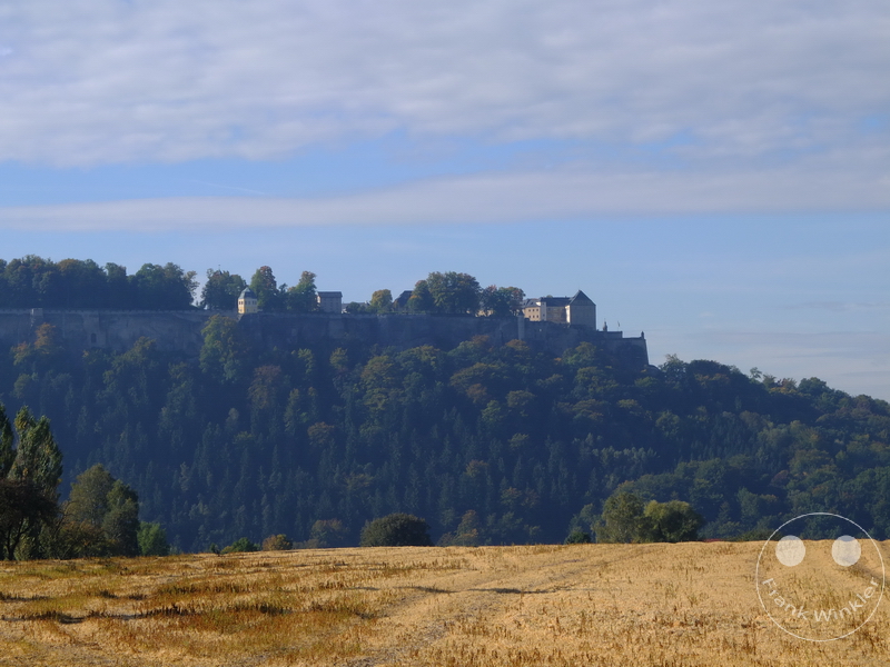 Deutschland - Festung Königstein auf bewaldetem Hügel mit weitem Feld und teils bewölktem Himmel im Hintergrund.