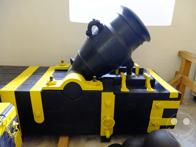 Deutschland - Festung Königstein - Historischer Mörser auf Holzwagen mit gelben Akzenten, Kanonenkugeln auf Holzboden innen.