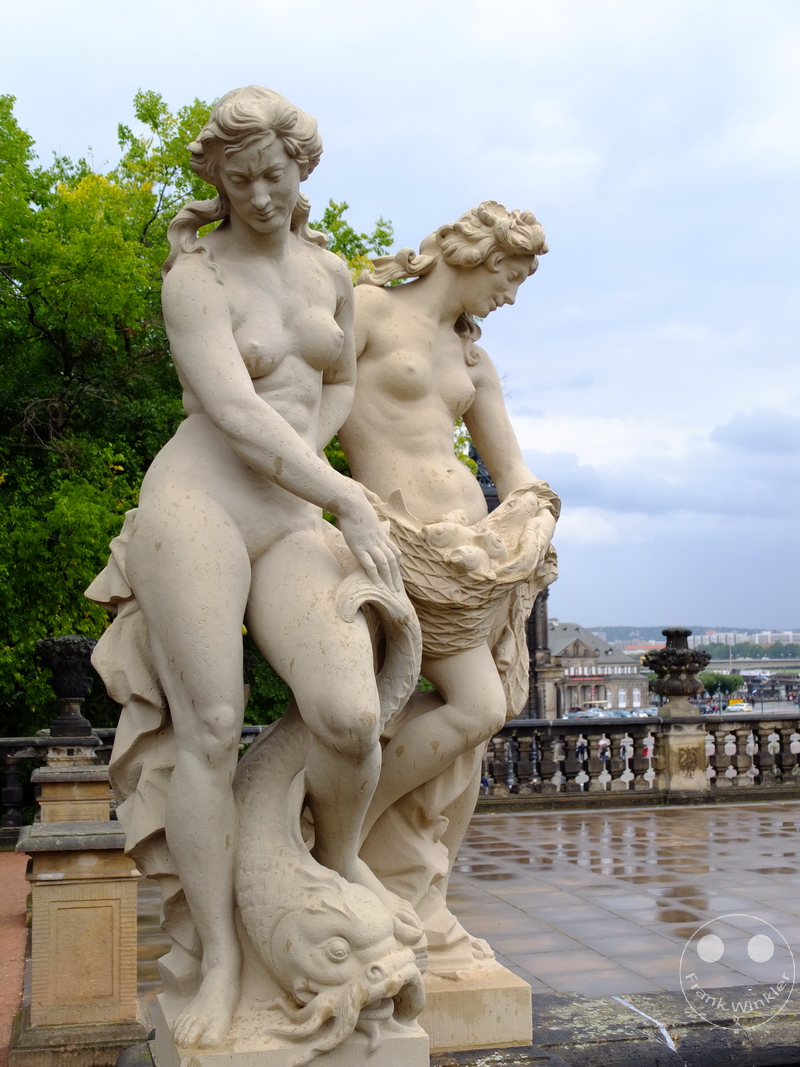 Deutschland - Dresden - Zwinger- Steinstatuen von Frauen mit Fisch, Bäume und Stadtlandschaft im Hintergrund.
