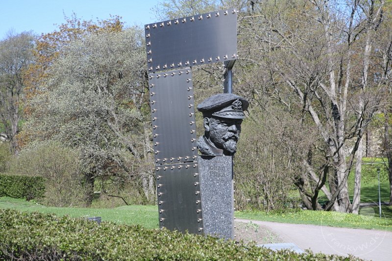 Estland - Tallinn - Bust of Johan Pitka - Skulptur eines kopfbedeckten Kopfes neben metallischer Struktur im Park mit Bäumen.