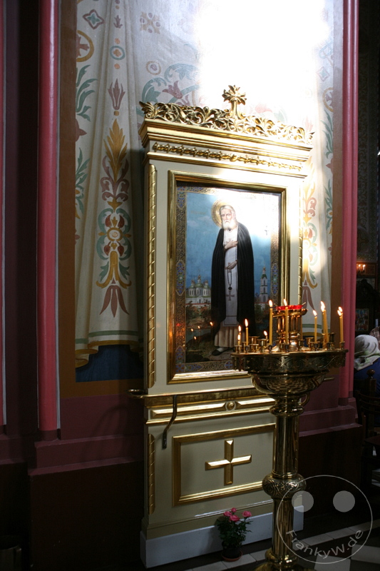 Estland - Tallinn - Ikone in vergoldetem Rahmen mit Kerzen auf Metallhalter vor dekorierter Wand.