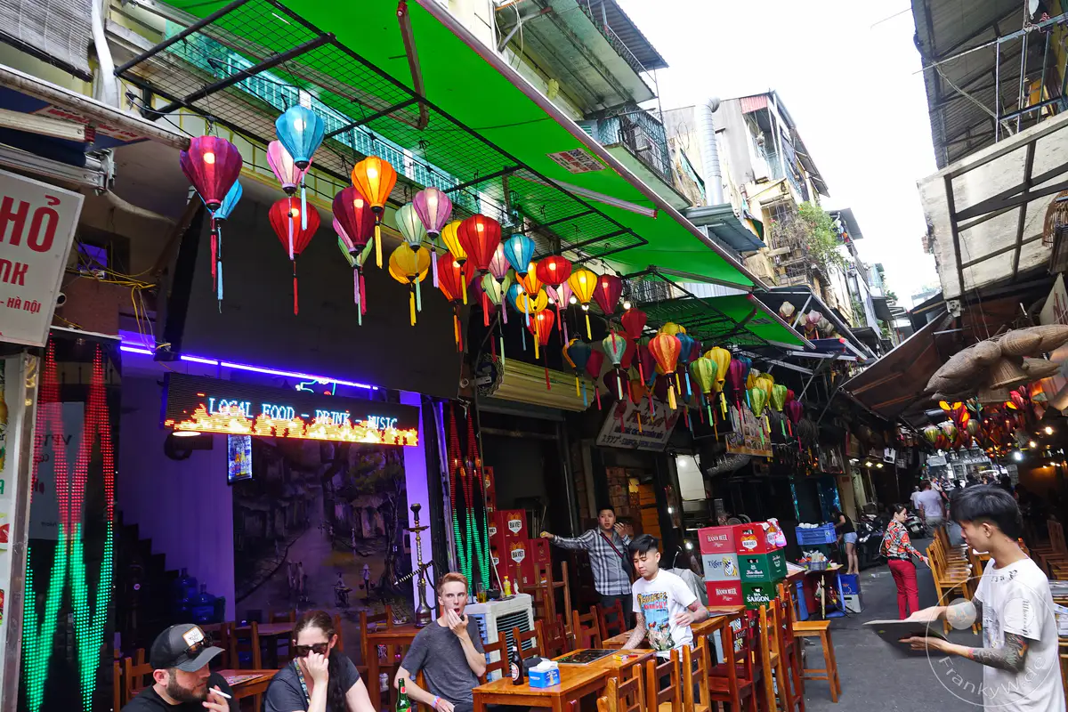 In Hanoi, Vietnam, dem belebten Old Quarter, herrscht ein reges Treiben bei Nacht. Bunte Papierlaternen und leuchtende Neonschilder erhellen die engen Gassen und laden zum Verweilen ein. Eine lebendige Atmosphäre aus Essen, Trinken und Musik erfüllt die Luft.