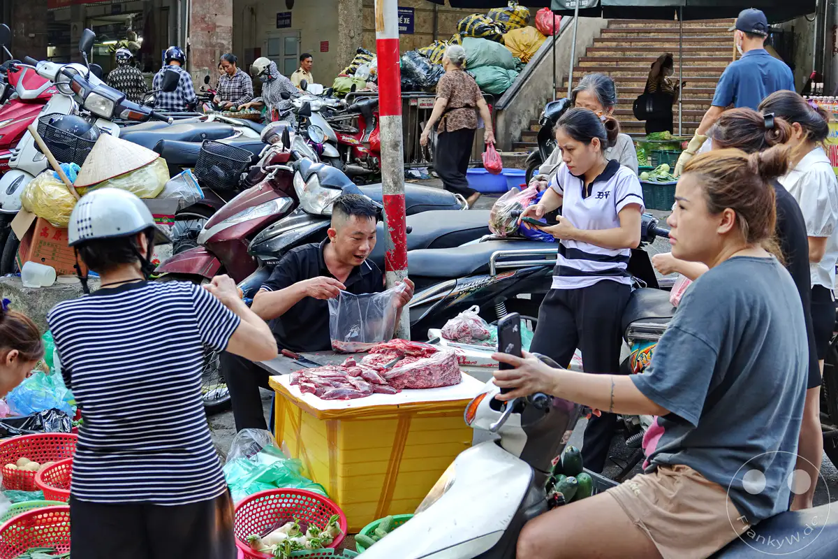 Auf dem geschäftigen Markt im Old Quarter von Hanoi in Vietnam bieten Händler frisches Fleisch und Gemüse an. Motorroller parken dicht gedrängt und unterstreichen die urbane Atmosphäre. Die Szene vermittelt einen Eindruck vom alltäglichen Leben und Treiben in dieser belebten asiatischen Metropole.