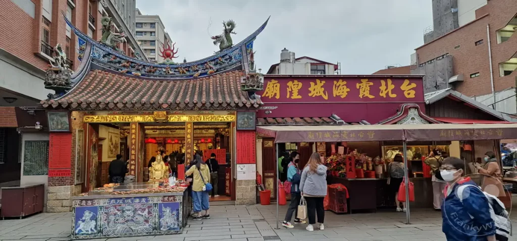 In Taipeh, Taiwan, präsentiert sich die Dihua Street mit einem traditionellen Tempel und einem belebten Markt. Menschenmengen drängen sich vor den Geschäften, während religiöse Symbole und bunte Dekorationen eine festliche Atmosphäre schaffen. Die Szene fängt die kulturelle Vitalität und das geschäftige Treiben dieser historischen Straße ein.