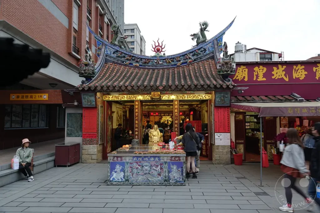 In Taipeh, Taiwan, erstreckt sich die belebte Dihua Street, flankiert von traditionellen Geschäften und einem Tempel, dessen ornate Dachkonstruktion auffällt. Im Vordergrund ist ein Opferaltar mit zahlreichen Räucherstäbchen zu sehen, während Besucher durch die Gasse flanieren. Die Szene vermittelt das geschäftige Treiben und die kulturelle Atmosphäre dieser historischen Handelsstraße.