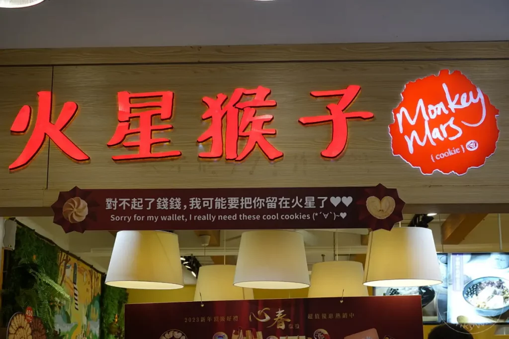 Eine rote Leuchtreklame in Taipeh, Taiwan, wirbt für "Monkey Mars Cookies" mit einer chinesischen und englischen Botschaft. Die Leuchtreklame, die einen stilisierten Affen im Weltraum mit "Monkey Mars (cookie)" darstellt, hängt über einem Geschäft in der Dihua Street. Unter der Leuchtreklame befindet sich eine weitere Botschaft, die auf Deutsch "Sorry for my wallet, I really need these cool cookies" lautet, was auf eine charmante und verspielte Marketingstrategie hinweist.
