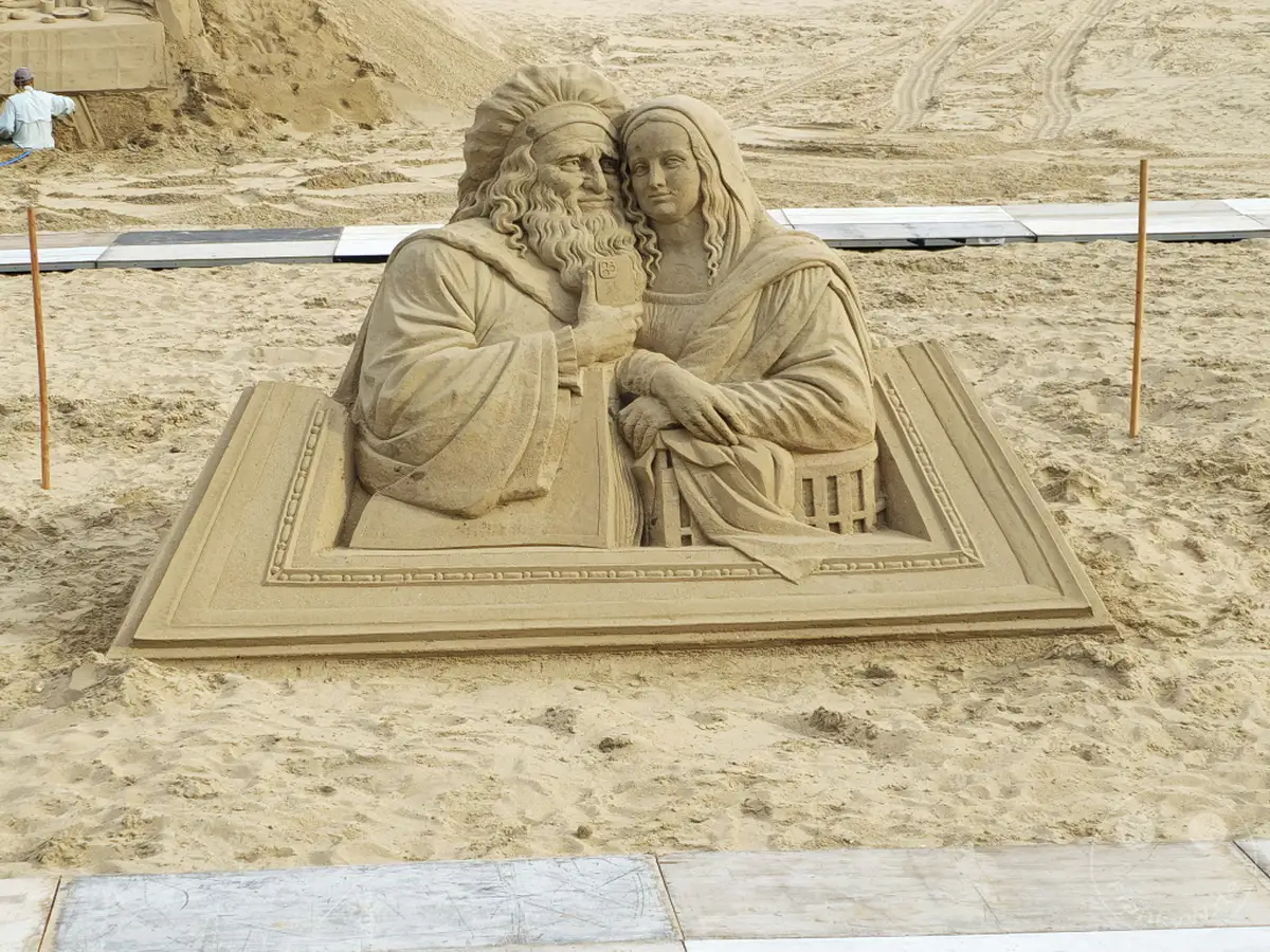 Eine beeindruckende Sandskulptur, die ein historisches Paar darstellt, ist am Haeundae Beach in Busan, Südkorea, ausgestellt. Das detailreiche Kunstwerk, das auf einem aufgeschlagenen Buch thront, zieht die Blicke der Strandbesucher auf sich. Die Szene vermittelt eine ruhige und künstlerische Atmosphäre inmitten des sonnigen Sandes.