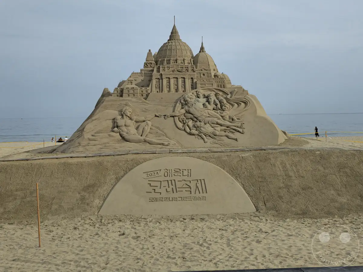 Ein monumentales Sandskulpturenkunstwerk, inspiriert von Michelangelos "Die Erschaffung Adams", thront am Haeundae Beach in Busan, Südkorea. Die detailreiche Nachbildung eines Renaissance-Gebäudes und menschlicher Figuren zieht die Blicke der Strandbesucher auf sich. Die friedliche Kulisse des Meeres und des Himmels unterstreicht die beeindruckende Kunstfertigkeit des temporären Bauwerks.
