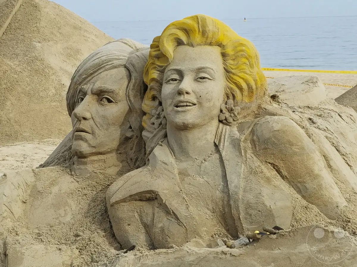 Sandskulpturen von bekannten Persönlichkeiten am Haeundae Beach in Busan, Südkorea, stellen ikonische Figuren dar. Die detailreiche Ausführung der Figuren, darunter Marilyn Monroe und ein Mann mit charakteristischem Haar, zeugt von künstlerischem Talent. Die Darstellung vor der Kulisse des Meeres und des Strandes schafft eine einzigartige und eindrucksvolle Szenerie.