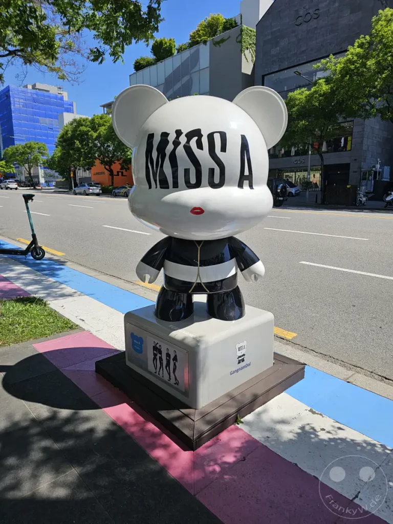 Eine auffällige Skulptur der Popgruppe "Miss A" steht stolz an der K-Star Road in Gangnam, Seoul, Südkorea. Die bunte Umgebung und die sonnige Atmosphäre der Straße spiegeln die lebendige Kultur des Viertels wider. Die Figur ist Teil der "GangnamDol"-Installation, die von Fans und Touristen gleichermaßen geschätzt wird.