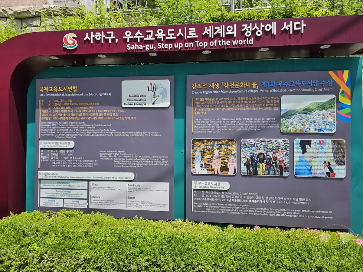 Die Tafel in Südkorea stellt das UNESCO-Programm „Educating Cities“ vor und hebt den „Gamcheon Culture Village“ hervor, der für seine Creative Regeneration ausgezeichnet wurde. Sie informiert über die Internationale Vereinigung der Bildungsstädte (IAEC) und ihre Netzwerke sowie die Auszeichnungen für herausragende Projekte. Die Darstellung vermittelt ein Gefühl von Stolz und Gemeinschaft im Zusammenhang mit städtischer Entwicklung und Bildung.