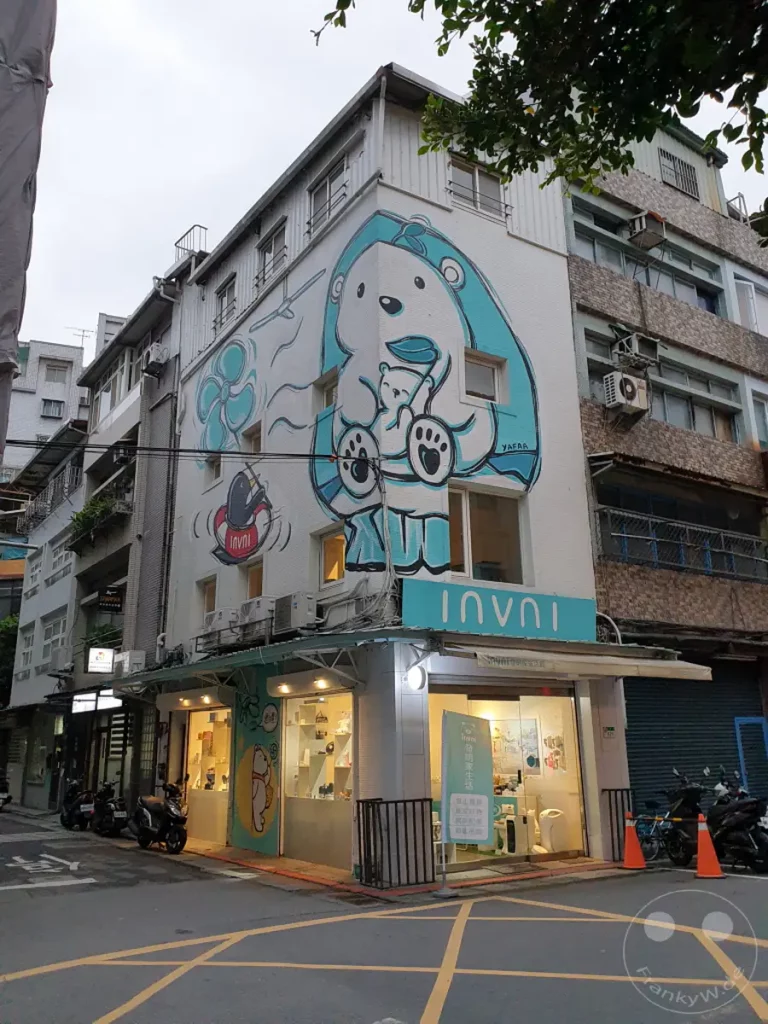 Ein Gebäude in der Dihua Street in Taipeh, Taiwan, ziert ein auffälliges Wandgemälde eines Eisbären. Davor befindet sich ein Geschäft mit einer bunten Auslage, das eine einladende Atmosphäre schafft. Die Szene kombiniert städtische Architektur mit künstlerischem Ausdruck.