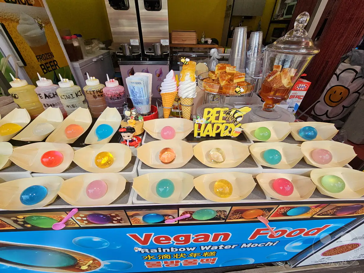 Im Culture Village Gamcheon in Busan, Südkorea, werden an einem Stand vielfältige Süßigkeiten wie bunte Mochi-Kugeln, Eis und Getränke angeboten. Die farbenfrohe und verspielte Präsentation lädt zum Probieren ein und vermittelt eine fröhliche Atmosphäre. Eine Auswahl an Eissorten und bunten Süßspeisen verspricht eine angenehme Erfrischung in der touristischen Umgebung.