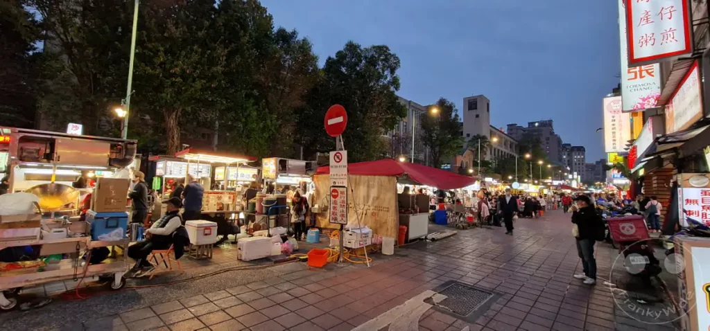 Eine geschäftige Nacht in Taipeh, Taiwan, wo der Ningxia Nightmarket bei Einbruch der Dunkelheit zum Leben erwacht. Garküchen reihen sich aneinander und bieten eine verlockende Auswahl an Streetfood, während Einheimische und Touristen die lebhafte Atmosphäre genießen. Das gedämpfte Licht und die Menschenmengen schaffen eine energiegeladene und einladende Stimmung.