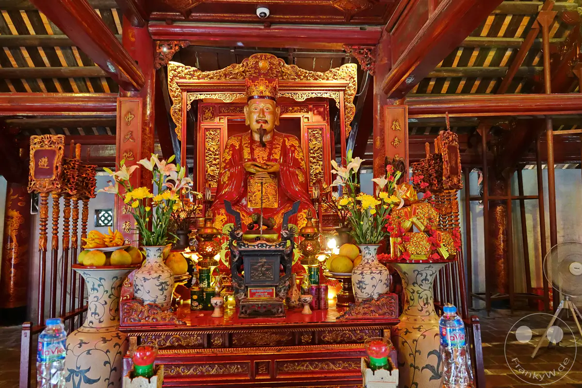 Im Inneren des Literaturtempels in Hanoi, Vietnam, thront eine prächtige Statue auf einem reich verzierten Altar. Umgeben von Blumen und Früchten strahlt die Szene eine tief spirituelle und kulturelle Atmosphäre aus. Die kunstvollen Holzschnitzereien und die leuchtenden Farben des Altars unterstreichen die historische Bedeutung dieses heiligen Ortes.