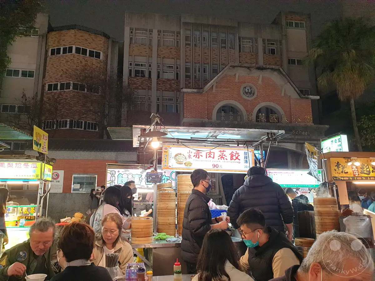 In Taipeh, Taiwan, herrscht am Ningxia Nightmarket reges Treiben, während die Nacht hereinbricht. Essensstände mit dampfenden Köstlichkeiten locken zahlreiche Besucher an, die sich durch die Gassen des belebten Marktes drängen. Die Szene ist erfüllt von der lebendigen Atmosphäre eines typischen Nachtmarktes, wo Einheimische und Touristen gemeinsam kulinarische Erlebnisse genießen.