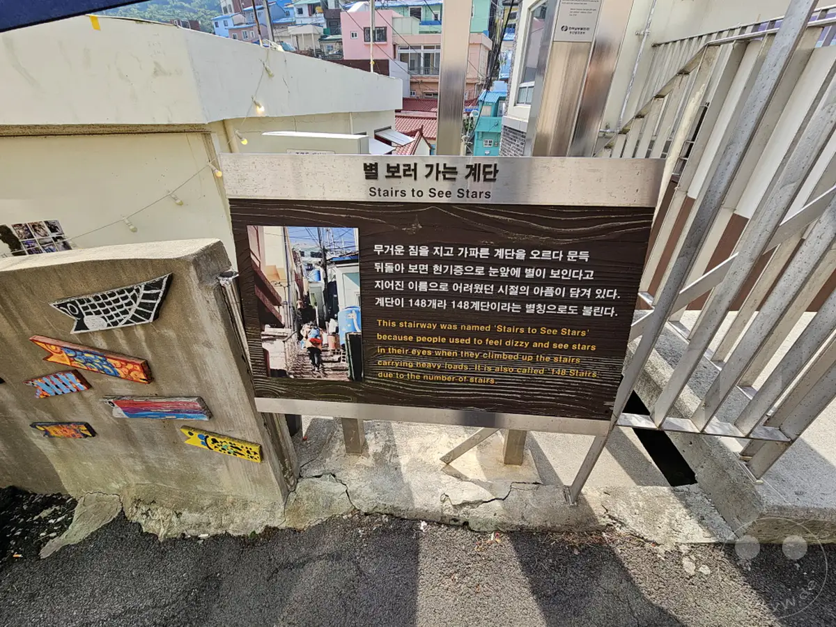 In Südkorea, Busan, befindet sich das Culture Village Gamcheon. Eine Treppe mit dem Namen 'Stairs to See Stars' ist mit künstlerischen Motiven geschmückt und erzählt die Geschichte des Ortes. Die Umgebung strahlt eine bunte und lebendige Atmosphäre aus, die von der lokalen Kultur geprägt ist.