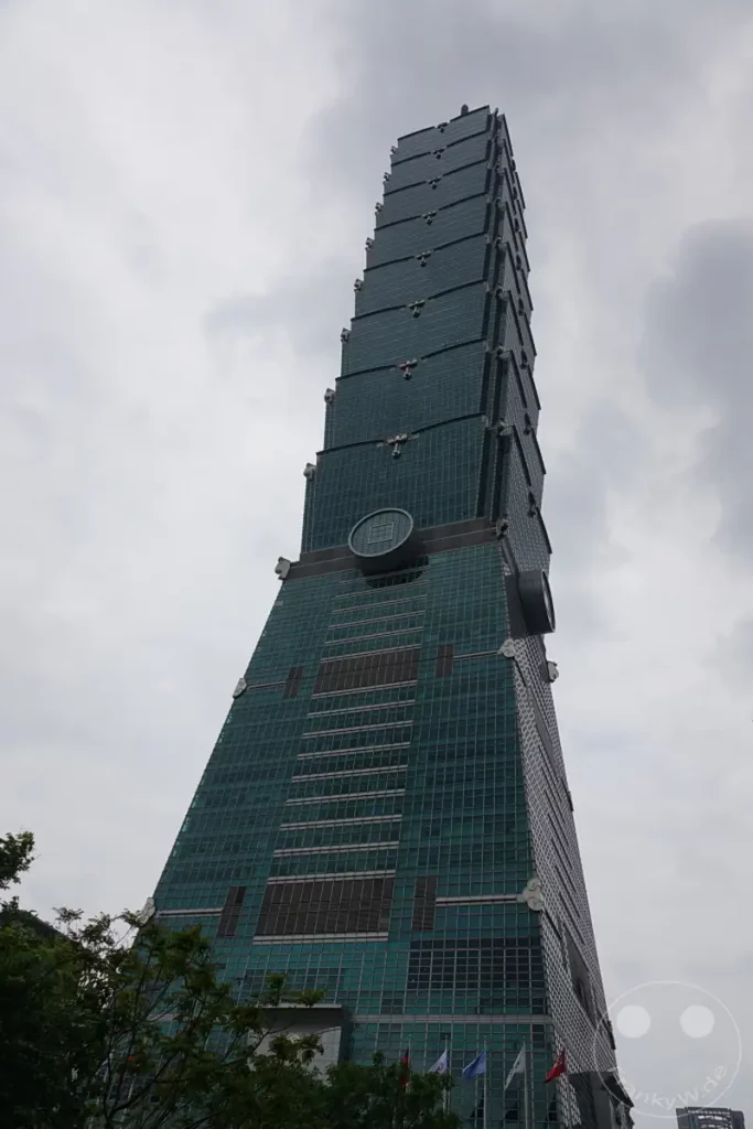 Der Taipei 101 ragt an einem bewölkten Tag imposant in den Himmel über Taipeh, Taiwan. Die markante, segmentierte Architektur des Wolkenkratzers ist von unten nach oben gut erkennbar. Die graue und diffuse Bewölkung verleiht der Aufnahme eine leicht melancholische, aber dennoch eindrucksvolle Atmosphäre.