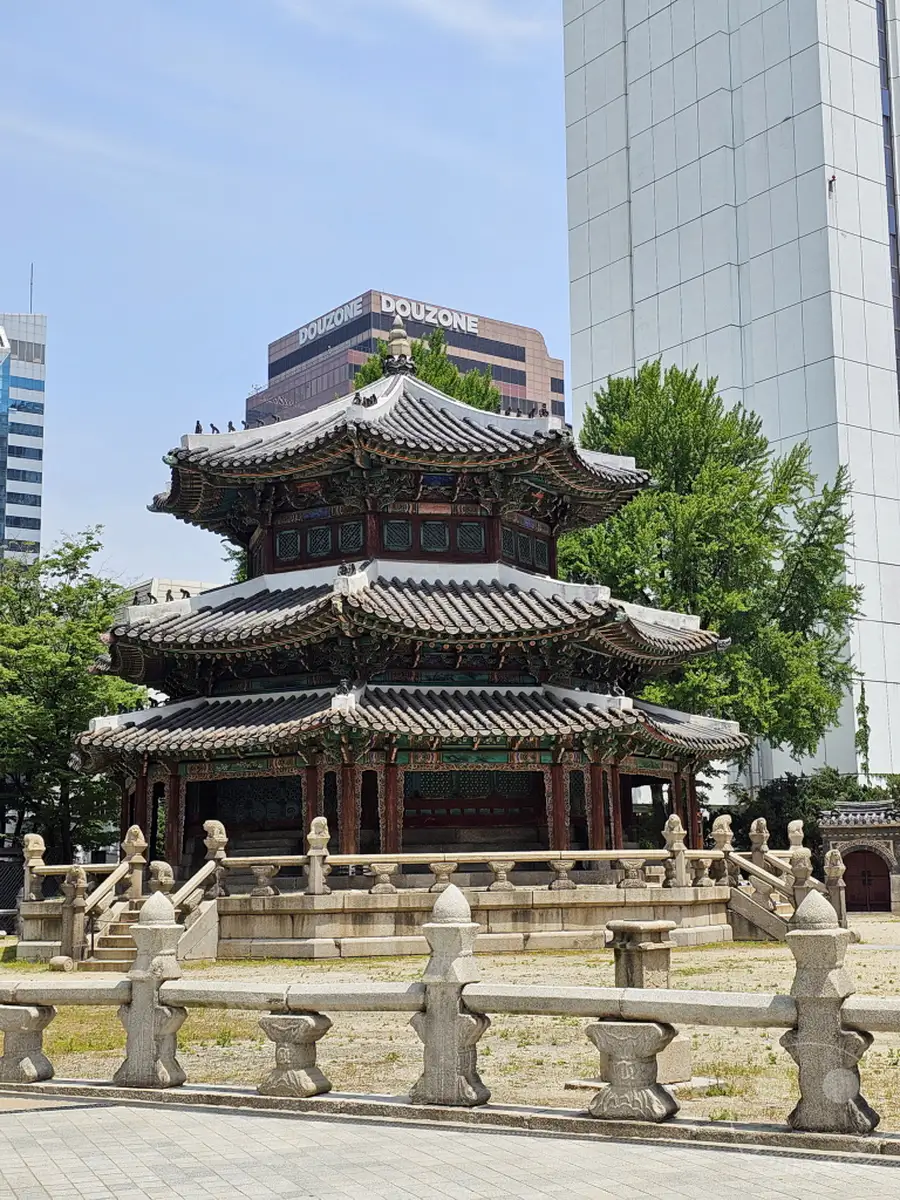 Ein detailreicher Blick auf eine traditionelle koreanische Pagode im Herzen von Seoul. Moderne Hochhäuser im Hintergrund bilden einen starken Kontrast zur historischen Architektur. Die Szene strahlt eine ruhige und zugleich imposante Atmosphäre aus, die die Verschmelzung von Alt und Neu in der südkoreanischen Hauptstadt zeigt, in der Nähe des Westin Josun Hotels.