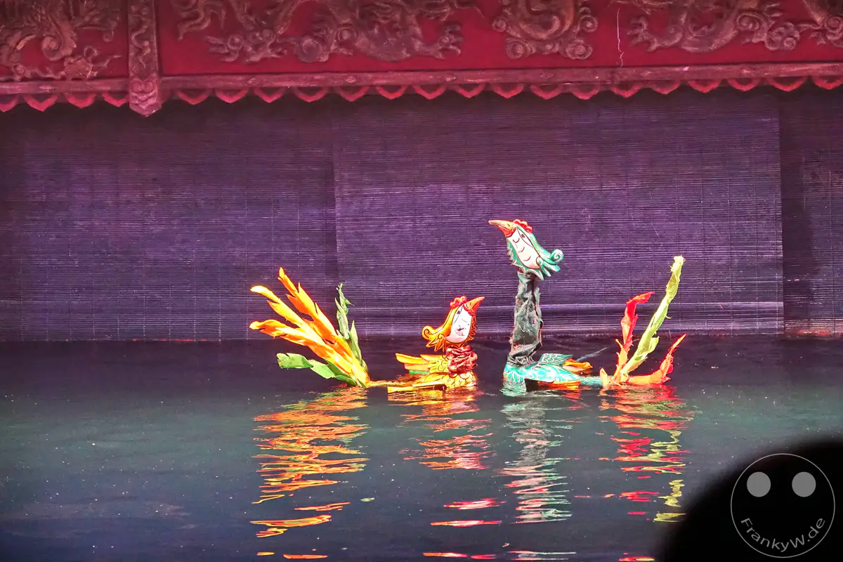 In Hanoi, Vietnam, wird eine traditionelle Wasserpuppenspiel-Aufführung präsentiert, bei der farbenfrohe Holzfiguren auf einer Wasserbühne agieren. Die Spiegelungen der beweglichen Puppen im dunklen Wasser erzeugen eine mystische und faszinierende Atmosphäre. Das bunte Zusammenspiel von Figuren und Licht auf der Wasseroberfläche fesselt die Zuschauer in dieser einzigartigen kulturellen Darbietung.