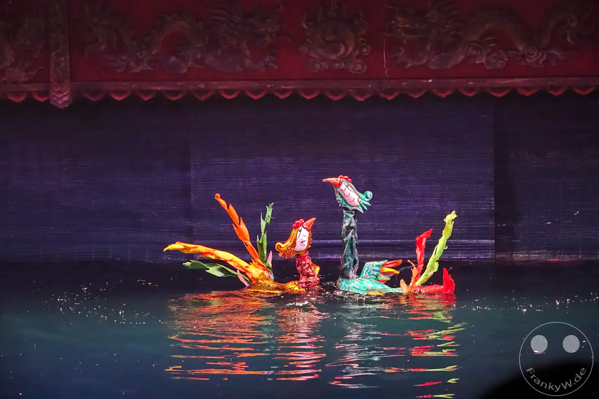 In Hanoi, Vietnam, wird eine faszinierende Vorstellung des Wasserpuppentheaters aufgeführt. Bunte Figuren, die an Drachen und Vögel erinnern, treiben auf dem Wasser und spiegeln sich in den Wellen. Die Atmosphäre ist von traditioneller Kunst und kulturellem Erbe geprägt.