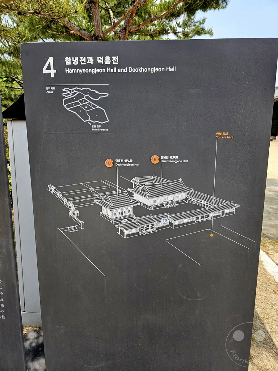 Ein schwarzes Informationstafel im Freien präsentiert eine Übersichtskarte des Deoksugung Palace in Seoul, Südkorea. Die Tafel ist in Koreanisch und Englisch beschriftet und zeigt die Standorte von Hamnyeongjeon Hall und Deokhongjeon Hall sowie die aktuelle Position des Betrachters. Der helle Himmel und die angedeutete Vegetation erzeugen eine klare und informative Atmosphäre für Besucher des Palastes.