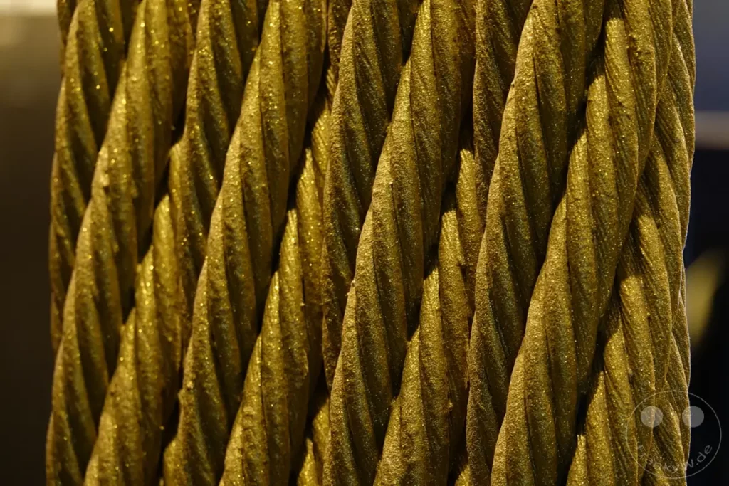 Eine makroaufnahme von goldenen, gedrehten Seilen offenbart eine faszinierende Textur mit glitzernden Partikeln. Das Licht spielt auf den verschiedenen Ebenen und erzeugt tiefe Schatten, die die spiralförmige Struktur hervorheben. Diese Detailaufnahme fängt die Pracht und den Glanz der Seile ein, die möglicherweise als dekoratives Element in Taipeh, Taiwan, verwendet werden.