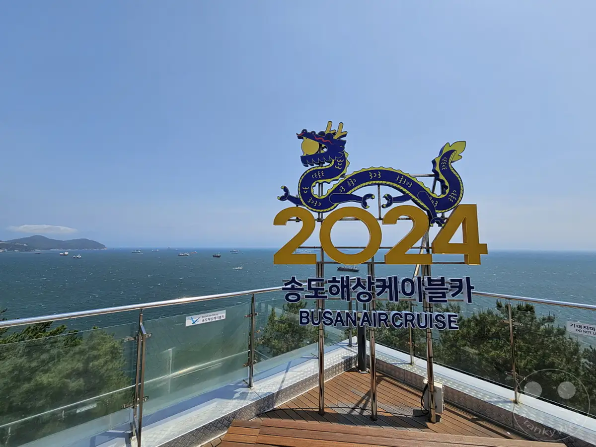 Die Seilbahn von Songdo in Busan, Südkorea, ist im Jahr 2024 mit einem prominenten Drachenmotiv geschmückt. Von der Aussichtsplattform genießt man einen weiten Blick über das Meer, das von zahlreichen Schiffen befahren wird. Die Szene vermittelt eine lebhafte und festliche Atmosphäre vor der Kulisse des blauen Himmels und des Meeres.