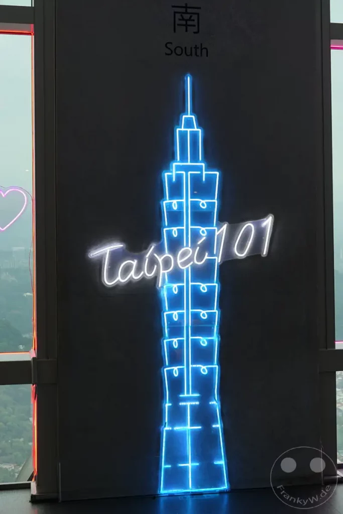 Neonlichter im modernen Stil beleuchten die Silhouette des ikonischen Taipei 101 Wolkenkratzers in Taipeh, Taiwan. Die leuchtenden blauen und weißen Linien des Kunstwerks stehen in starkem Kontrast zur dunklen Wand und der verschwommenen Stadtansicht im Hintergrund. Eine stimmungsvolle Darstellung des Wahrzeichens, die sowohl die architektonische Eleganz als auch die pulsierende Atmosphäre der Stadt einfängt.