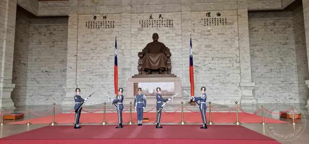 Soldaten in Uniformen führen eine Wachablösungszeremonie vor der Chiang Kai-shek Memorial Hall in Taipeh, Taiwan, durch. Die ernste Haltung der Wachsoldaten und die imposante Architektur der Gedenkstätte erzeugen eine würdevolle und respektvolle Atmosphäre. Die Szene fängt die Disziplin und denIONALen Stolz ein, der mit solchen Zeremonien verbunden ist.
