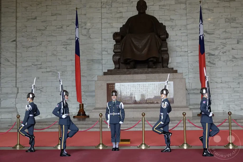 Die Chiang Kai-shek Memorial Hall in Taipeh, Taiwan, ist Schauplatz einer feierlichen Wachablösung vor dem Denkmal des ehemaligen Präsidenten. Mehrere Wachsoldaten in Uniformen präsentieren sich in einer synchronisierten Formation. Die sterile Marmorarchitektur bildet einen imposanten Hintergrund für die militärische Zeremonie.