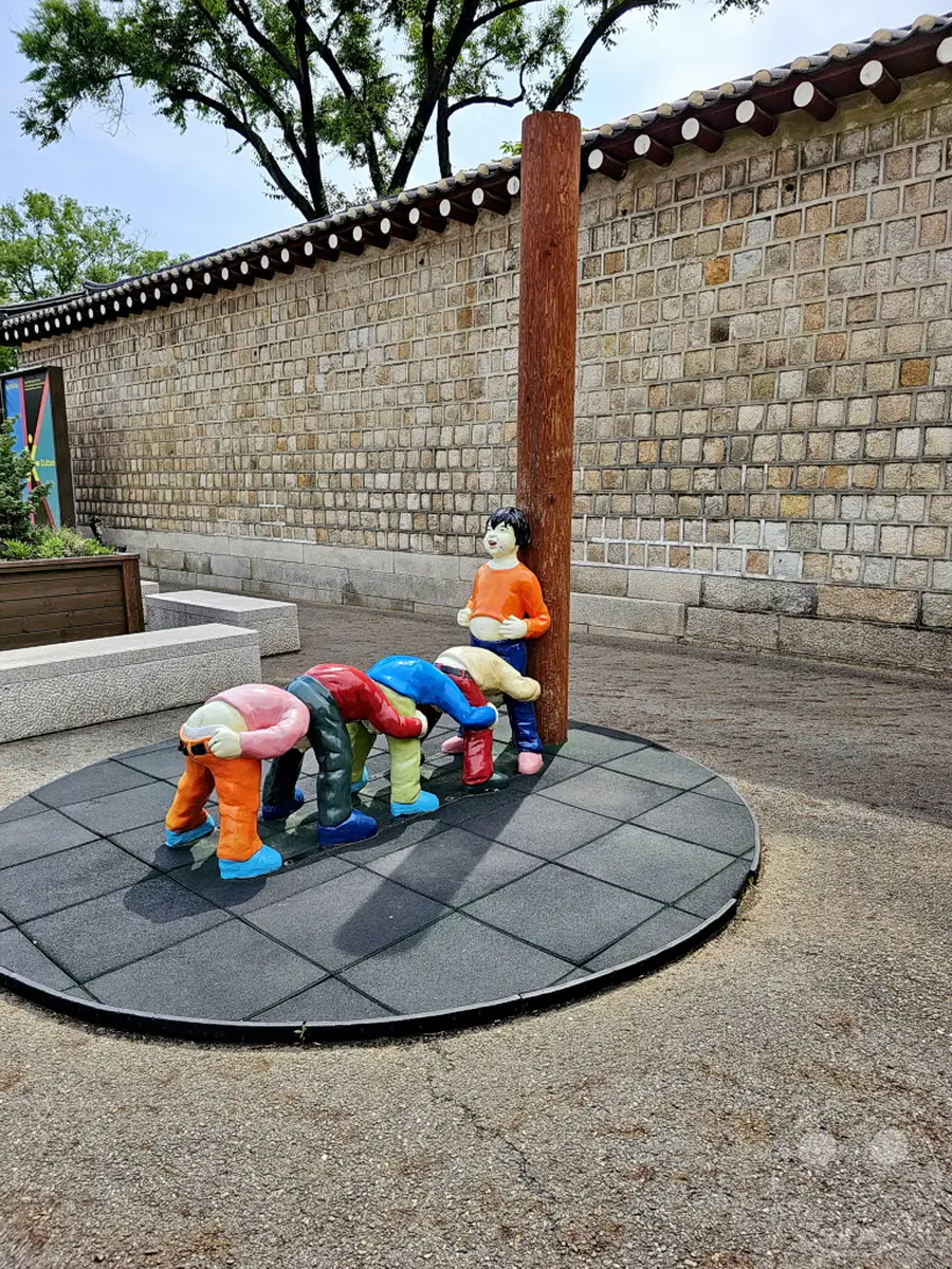 Im Herzen von Seoul, Südkorea, befindet sich ein Spielbereich im Gyeongbokgung Palace, der eine einzigartige Skulpturengruppe für Kinder bietet. Die bunten Figuren laden zu spielerischem Entdecken ein und fügen sich harmonisch in die historische Kulisse ein. Die Szene vermittelt eine Atmosphäre der Freude und des kulturellen Miteinanders, wo alte Tradition auf moderne Freizeitgestaltung trifft.
