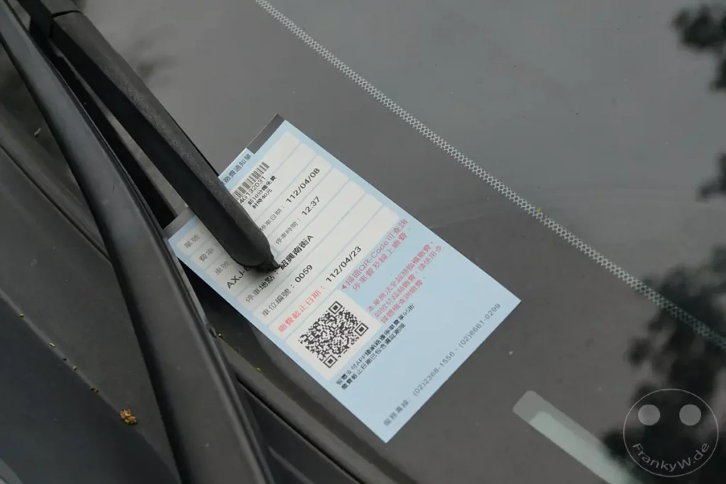 Ein Strafzettel wegen Parkgebühren klebt an einer Windschutzscheibe in Taipeh, Taiwan. Das Dokument informiert über die Parkdauer und Gebühren und enthält einen QR-Code zur Bezahlung. Die Szene vermittelt einen alltäglichen Eindruck des Stadtlebens und der Parkraumbewirtschaftung.