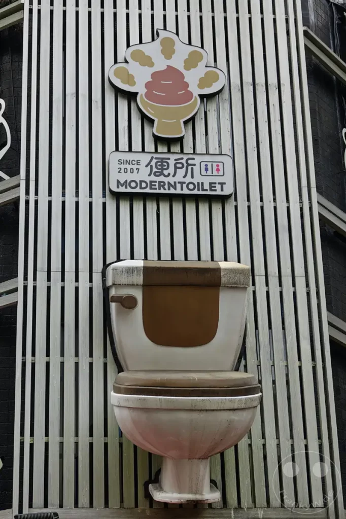 Eine ungewöhnliche Toiletten-Skulptur, die wie ein Eisbecher mit Kotze aussieht, ziert die Fassade eines Restaurants in Taipeh, Taiwan. Das Kunstwerk ist mit dem Schriftzug "Since 2007 ModernToilet" versehen und schafft eine humorvolle und auffällige Atmosphäre.