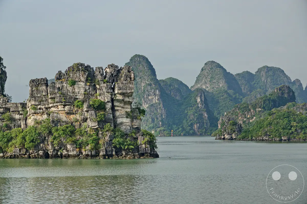 Die Ha Long Bucht in Vietnam präsentiert sich mit einer atemberaubenden Landschaft aus majestätischen Karstfelsen, die aus dem ruhigen Wasser des Meeres emporragen. Dichte grüne Vegetation bedeckt die Spitzen vieler dieser geologischen Wunder, während der Himmel leicht bewölkt ist und eine friedliche Atmosphäre schafft. Dieses Bild fängt die majestätische Schönheit und die natürliche Erhabenheit der Bucht ein, die zum Erkunden und Staunen einlädt.