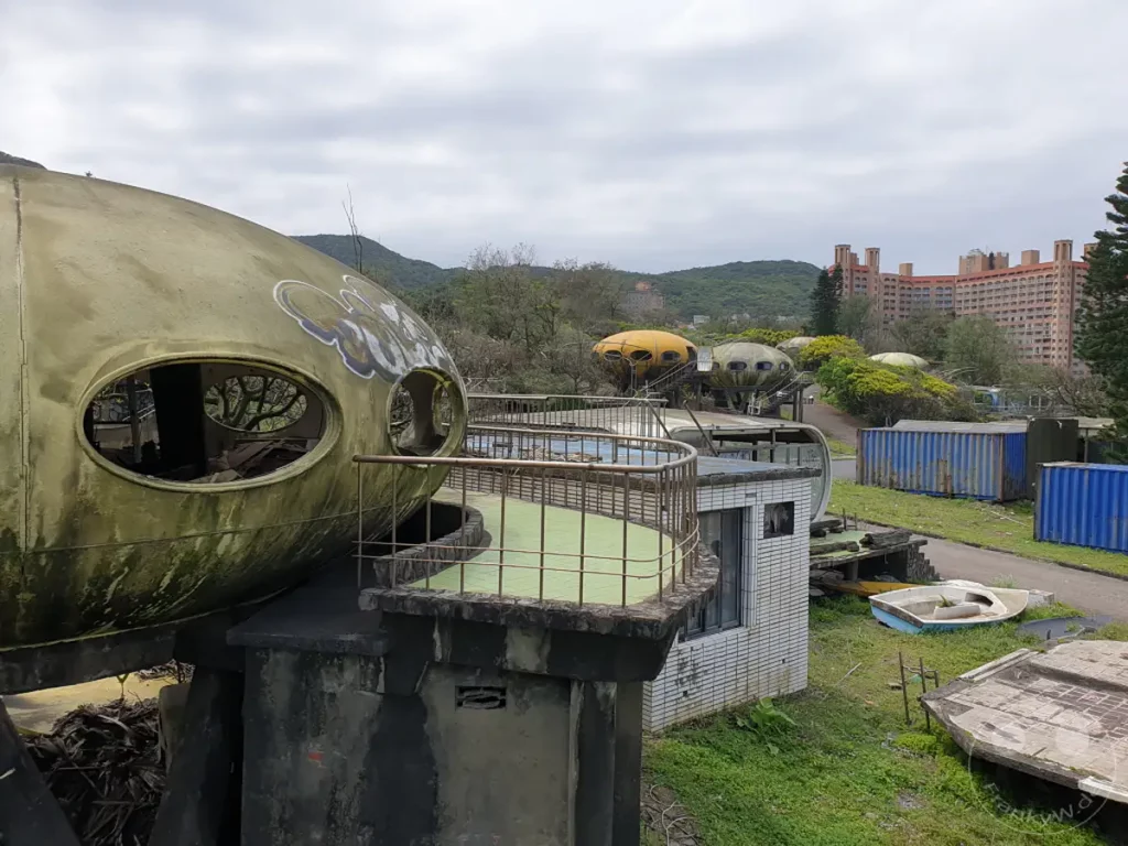 Überreste des verlassenen UFO Village in Wanli, Taiwan, mit seinen charakteristischen, futuristischen Futuro-Häusern, die im Verfall begriffen sind. Die Szenerie strahlt eine melancholische Atmosphäre der Vergänglichkeit und des vergangenen Traums aus. Zwischen überwucherter Vegetation und rostigen Strukturen bietet sich ein eindringlicher Anblick der Natur, die sich ihren Raum zurückerobert.