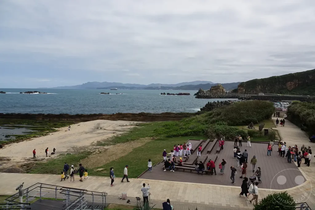 Besucher spazieren entlang der Küste des Yehliu Geoparks in Taiwan, wo sie die einzigartigen geologischen Formationen bestaunen. Das Meer und die felsige Landschaft schaffen eine atemberaubende Kulisse für den Ausflug. Die Menschen genießen die Aussicht und das Erkunden der bemerkenswerten Naturwunder.