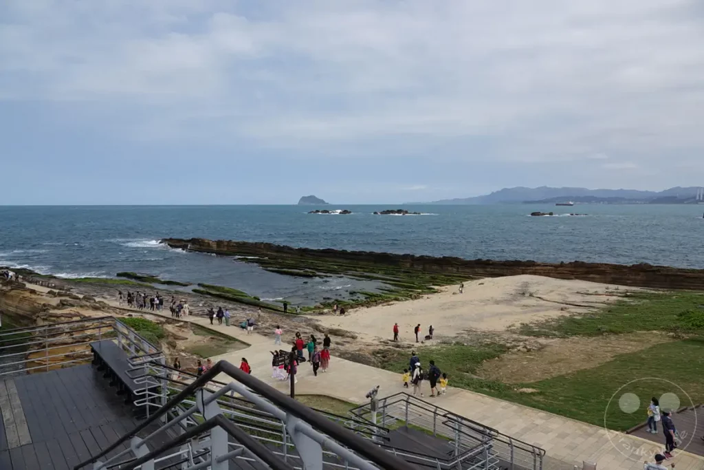 Die Küstenlandschaft des Yehliu Geoparks in Taiwan präsentiert sich mit einzigartigen Felsformationen, die vom Meer umspült werden. Besucher erkunden die Wege entlang der zerklüfteten Küste, während die Wellen gegen die Steine schlagen. Eine malerische Szenerie mit beeindruckenden geologischen Wundern unter einem bewölkten Himmel.
