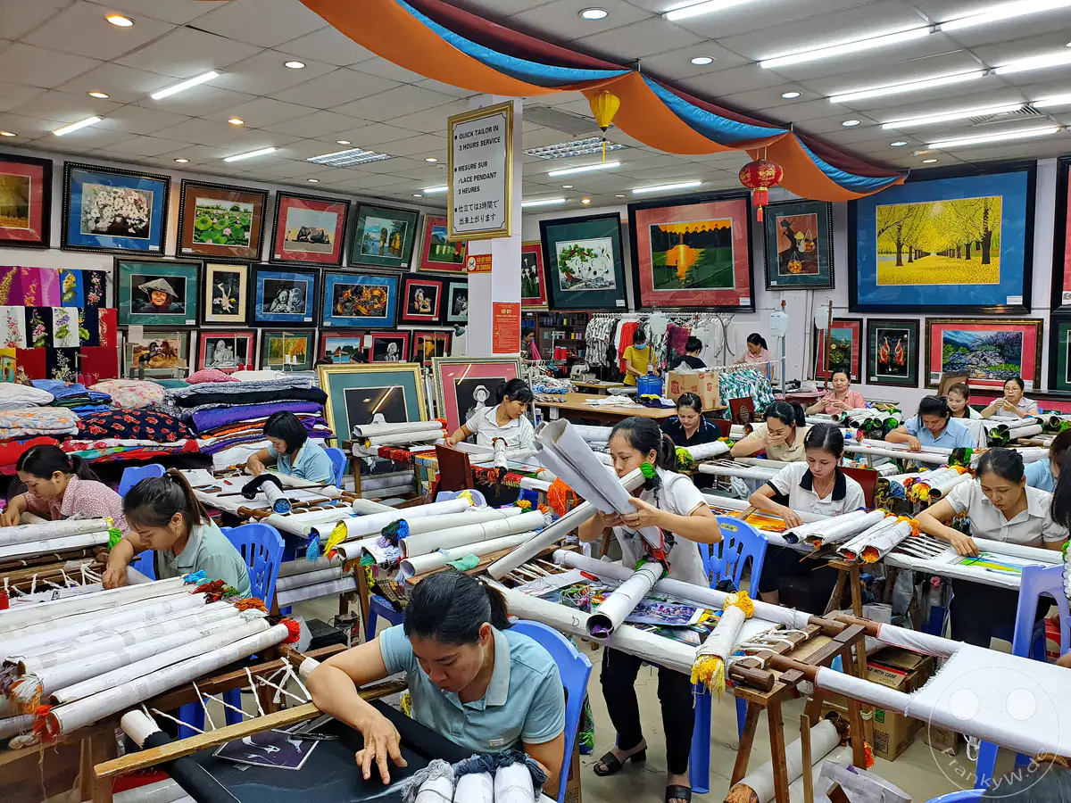 In einer Werkstatt in Dai Bat, Vietnam, konzentrieren sich Frauen auf kunstvolle Stickereien. Bunte Fäden und Stoffe umgeben die fleißigen Hände, während traditionelle Handwerkskunst zum Leben erweckt wird. Die Szene strahlt eine Atmosphäre konzentrierter Kreativität und handwerklichen Könnens aus.