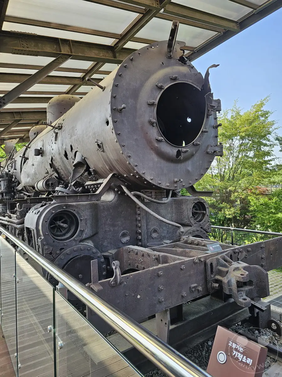 Eine zerstörte Dampflokomotive, ein Zeugnis des Koreakriegs, steht unter einem schützenden Vordach in der Nähe der Demilitärisierten Zone (DMZ) in Südkorea. Die verrosteten und durch Einschüsse gezeichneten Überreste strahlen eine beklemmende Atmosphäre aus und erinnern an die Schrecken des Konflikts. Das historische Artefakt bietet einen bedrückenden Einblick in die Vergangenheit des Landes.