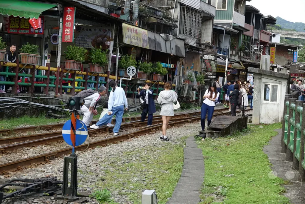 Menschenmassen bewegen sich auf den Eisenbahnschienen entlang der belebten Jiufen Old Street in Taiwan. Händler bieten Waren aus kleinen Läden und Ständen an, während Touristen die einzigartige Atmosphäre genießen. Die Szenerie fängt das geschäftige Treiben und den Charme dieses beliebten Reiseziels ein.