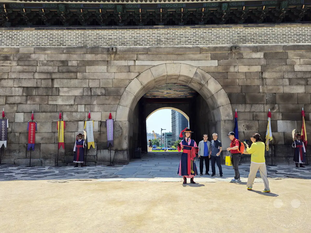 Vor dem historischen Sungnyemun Gate in Seoul, Südkorea, findet eine traditionelle Wachablösungszeremonie statt. Touristen beobachten die Darsteller in farbenfroher hanbok-Kleidung. Die Szene vermittelt ein Gefühl von kulturellem Erbe und historischer Bedeutung.