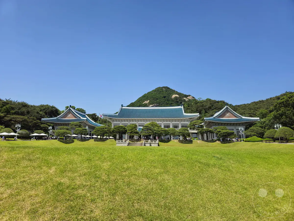 Die beeindruckende Architektur des Blauen Hauses (Cheongwadae) in Seoul, Südkorea, wird von einem üppigen Grün und einem strahlend blauen Himmel eingerahmt. Das historische Gebäude mit seinen charakteristischen blauen Dächern steht als Symbol der koreanischen Präsidentschaft und strahlt eine Atmosphäre der Würde und Geschichte aus. Besucher genießen die weitläufige Rasenfläche und die gepflegten Bäume, die zur Entspannung und Besichtigung einladen.