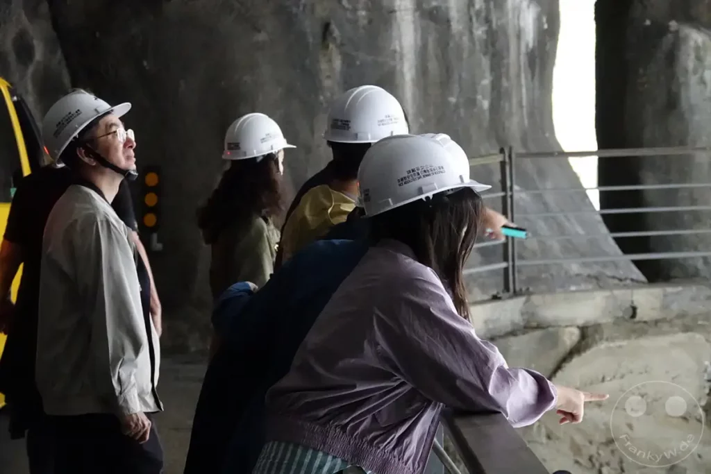 Eine Gruppe von Touristen trägt Schutzhelme, während sie eine Führung durch einen Tunnel im Taroko Nationalpark in Taiwan macht. Die raue Felswand und das gedämpfte Licht schaffen eine eindringliche Atmosphäre für die Entdeckung der natürlichen Geologie. Die aufmerksamen Besucher sind auf die Ausführungen des Reiseleiters konzentriert.