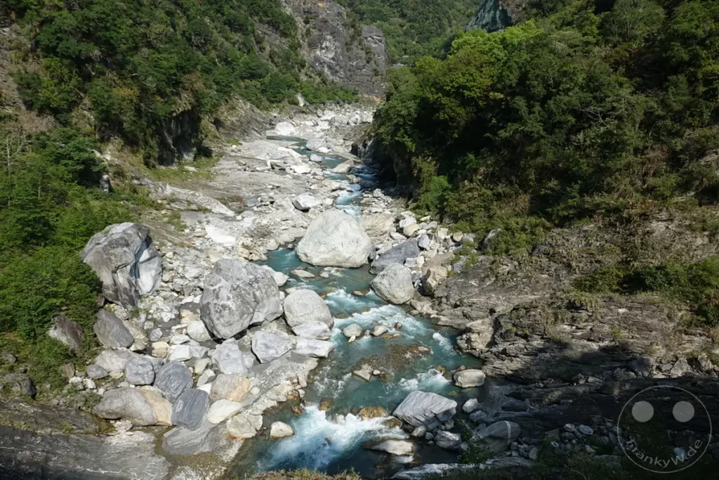 Der Taroko Nationalpark in Taiwan präsentiert sich mit dem Yuewangting-Abschnitt, wo ein türkisblauer Fluss sich seinen Weg durch eine tiefe Schlucht bahnt. Zahlreiche Felsformationen säumen das Ufer und spiegeln die raue Schönheit der Gebirgslandschaft wider. Die Szene vermittelt ein Gefühl von Erhabenheit und unberührter Natur.
