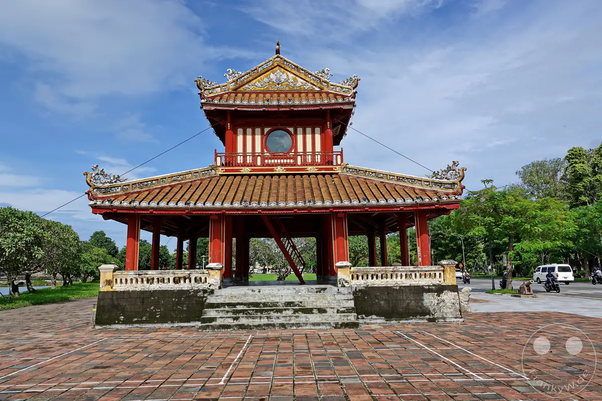 Die Thien Mu Pagode in Hue, Vietnam, erhebt sich majestätisch unter einem strahlend blauen Himmel mit vereinzelten Wolken. Die traditionelle Architektur mit ihren geschwungenen Dächern und reich verzierten Details strahlt Ruhe und Erhabenheit aus. Die friedliche Atmosphäre wird nur durch das entfernte Rauschen des Verkehrs durchbrochen, was einen Kontrast zwischen Geschichte und Moderne bildet.