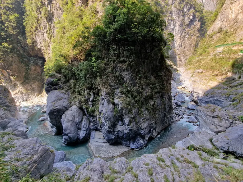 Eine tiefe Schlucht im Taroko Nationalpark in Taiwan offenbart einen türkisfarbenen Fluss, der sich durch bizarre Felsformationen schlängelt. Üppige Vegetation bedeckt die steilen Felswände, während Sonnenlicht die Szenerie dramatisch in Szene setzt. Die Majestät der Natur und die Formgebung des Tunnels sind eindrucksvoll zu erkennen.