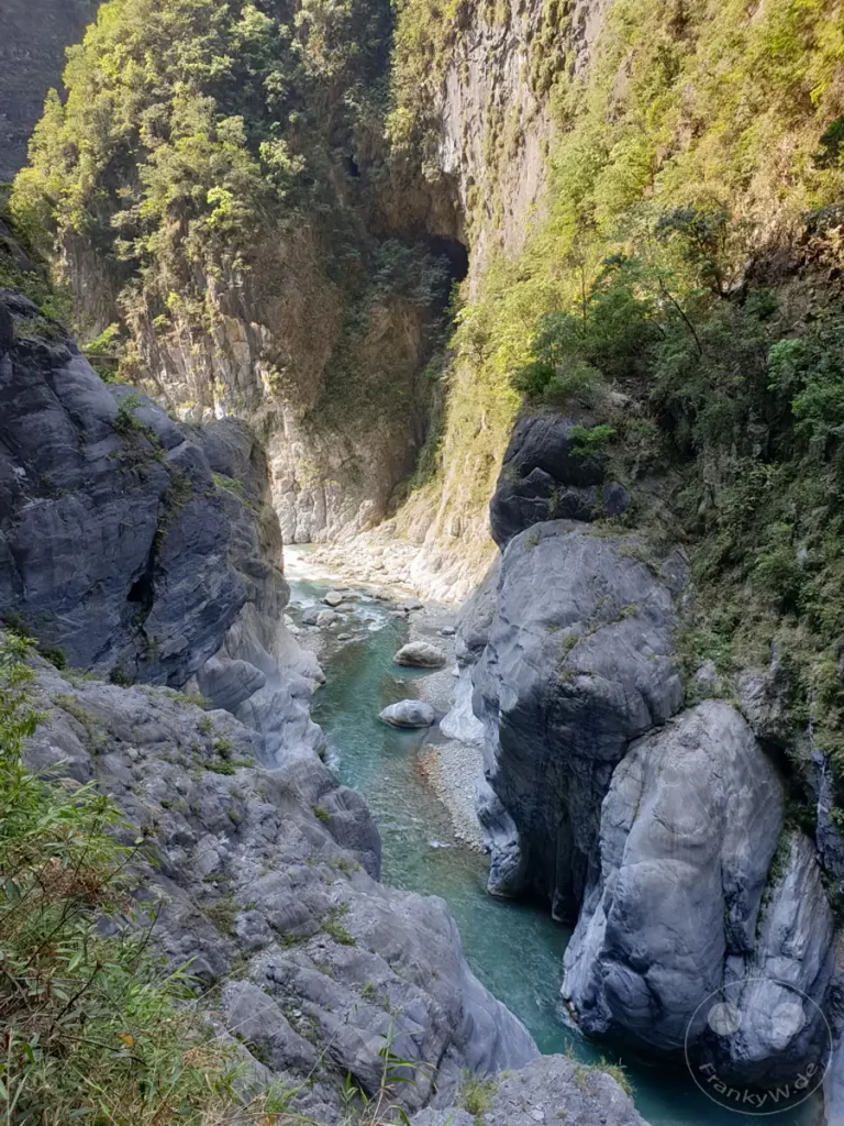 Eine türkisfarbene Wasserstraße schlängelt sich durch die tiefen Schluchten des Taroko Nationalparks in Taiwan. Majestätische, von der Erosion geformte Felswände ragen steil empor und werden von üppiger Vegetation bedeckt. Die Szenerie strahlt eine beeindruckende Ruhe und unberührte Naturkraft aus, die den Blick auf die gewaltigen Formationen wie den Tunnel of Nine Turns lenkt.